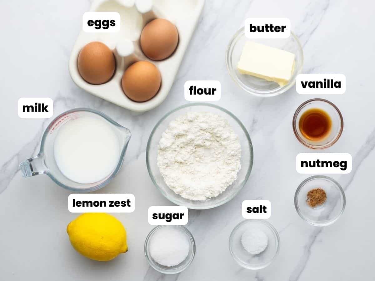 All of the ingredients needed to make Dutch Baby pancake, in separate small bowls, arranged on a marble counter.