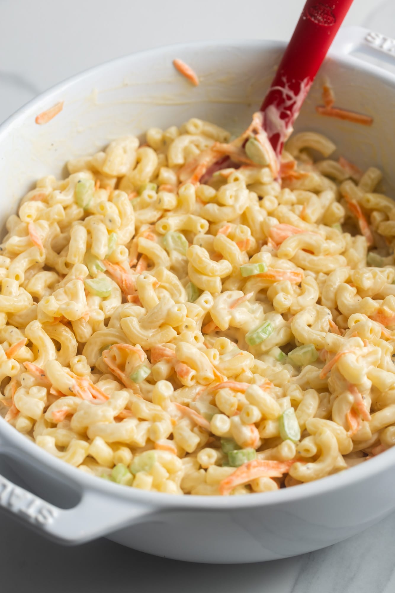 stirring dressing into elbow noodles and vegetables to make macaroni salad.