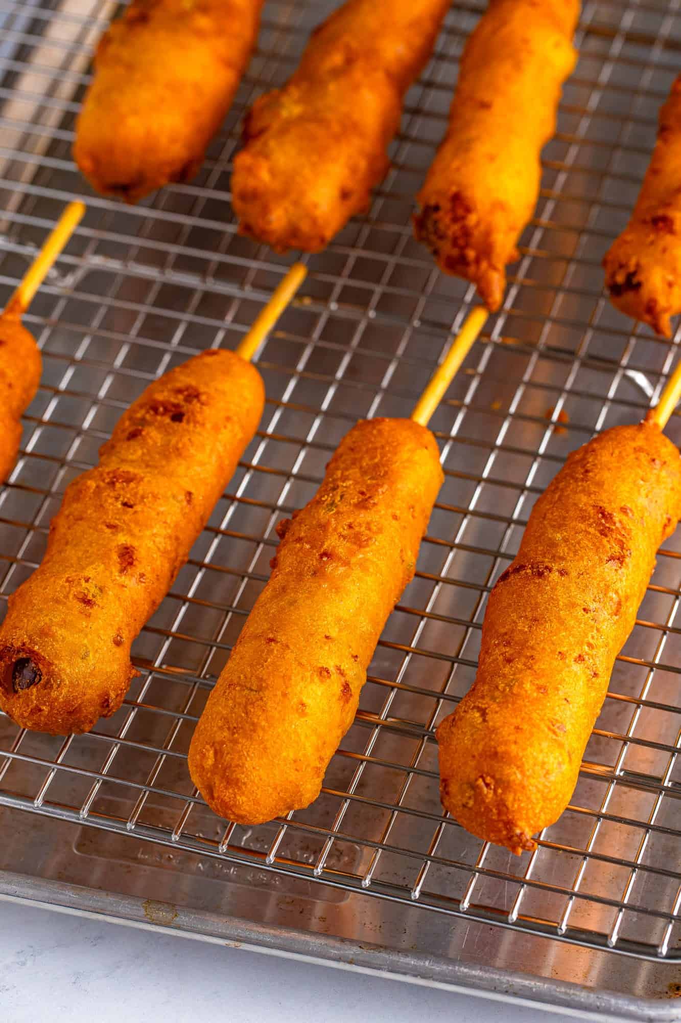 a wire rack holding fried homemade corn dogs over a sheet tray.