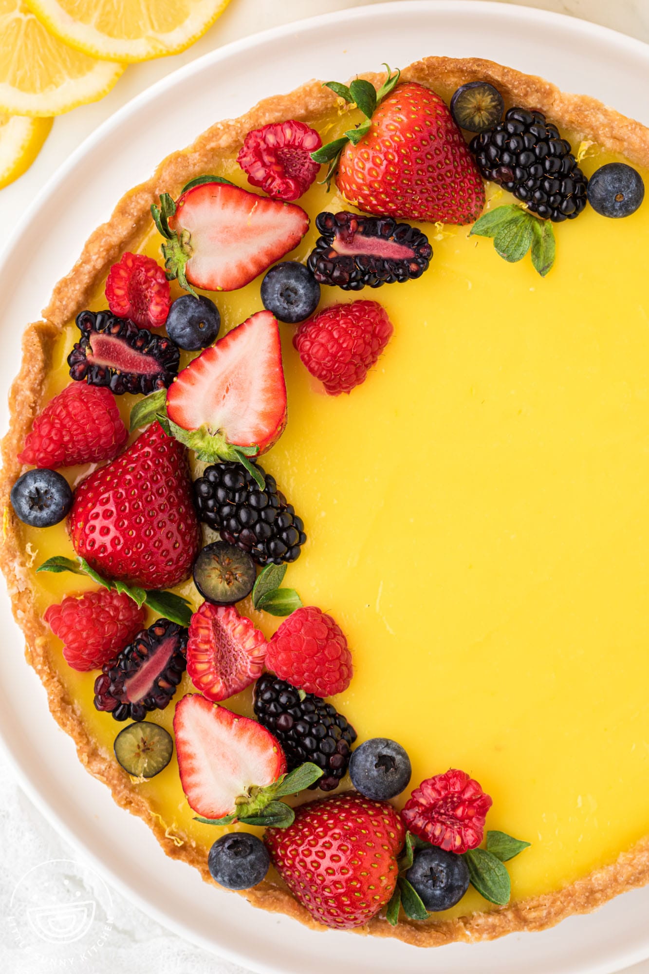 Overhead shot of a beautiful yellow lemon tart with shortbread crust, topped with fresh berries and viewed from above. 