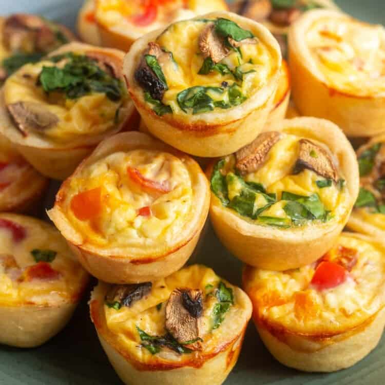 a green ceramic plate holding stacked mini quiches filled with veggies.