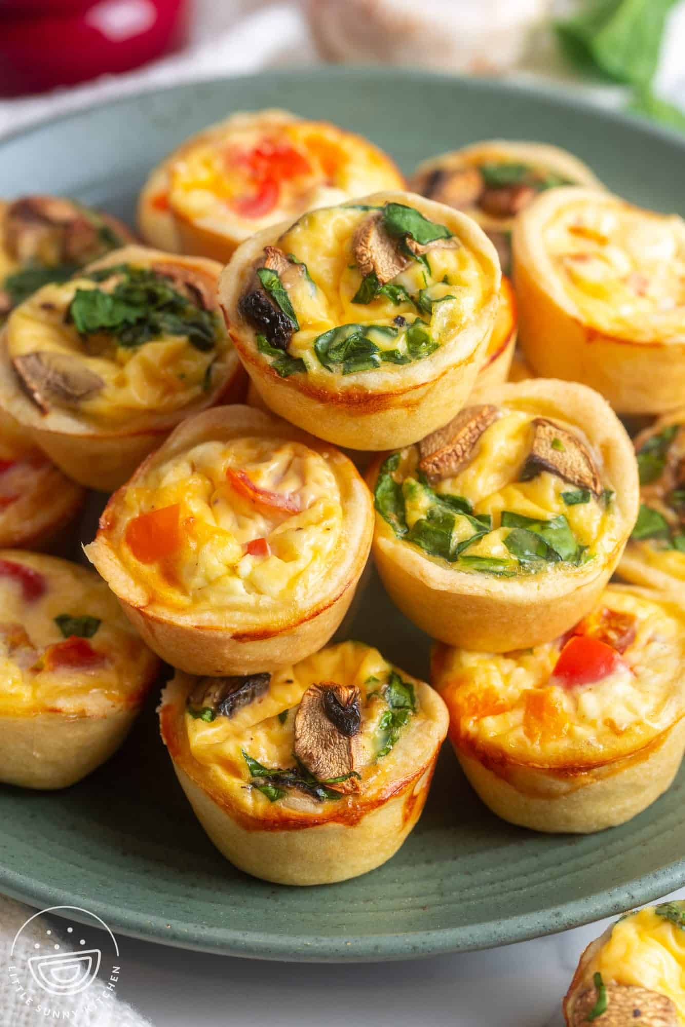 a green ceramic plate holding stacked mini quiches filled with veggies.