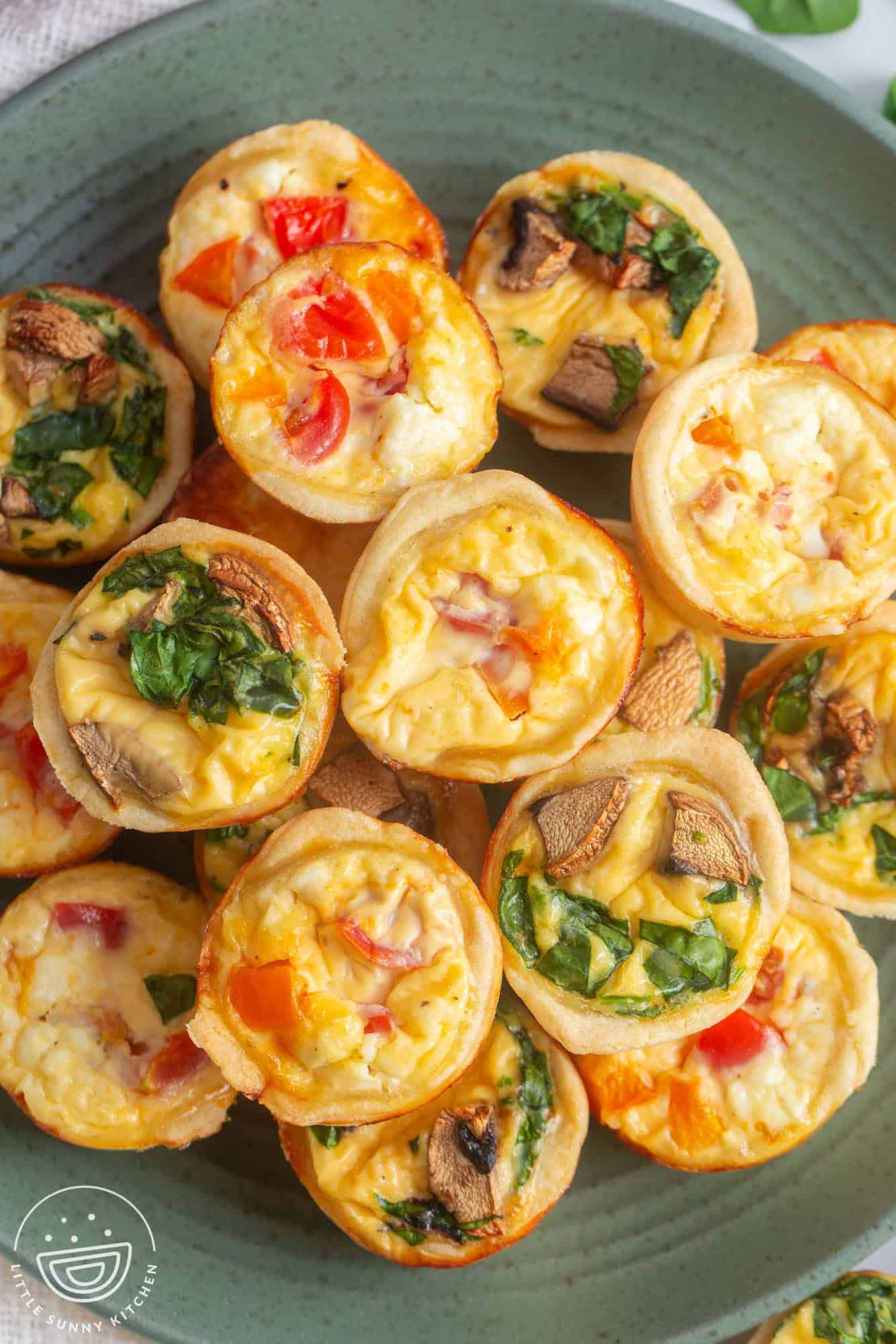 Mini quiche filled with veggies and cheese, stacked on a green plate, viewed from above.
