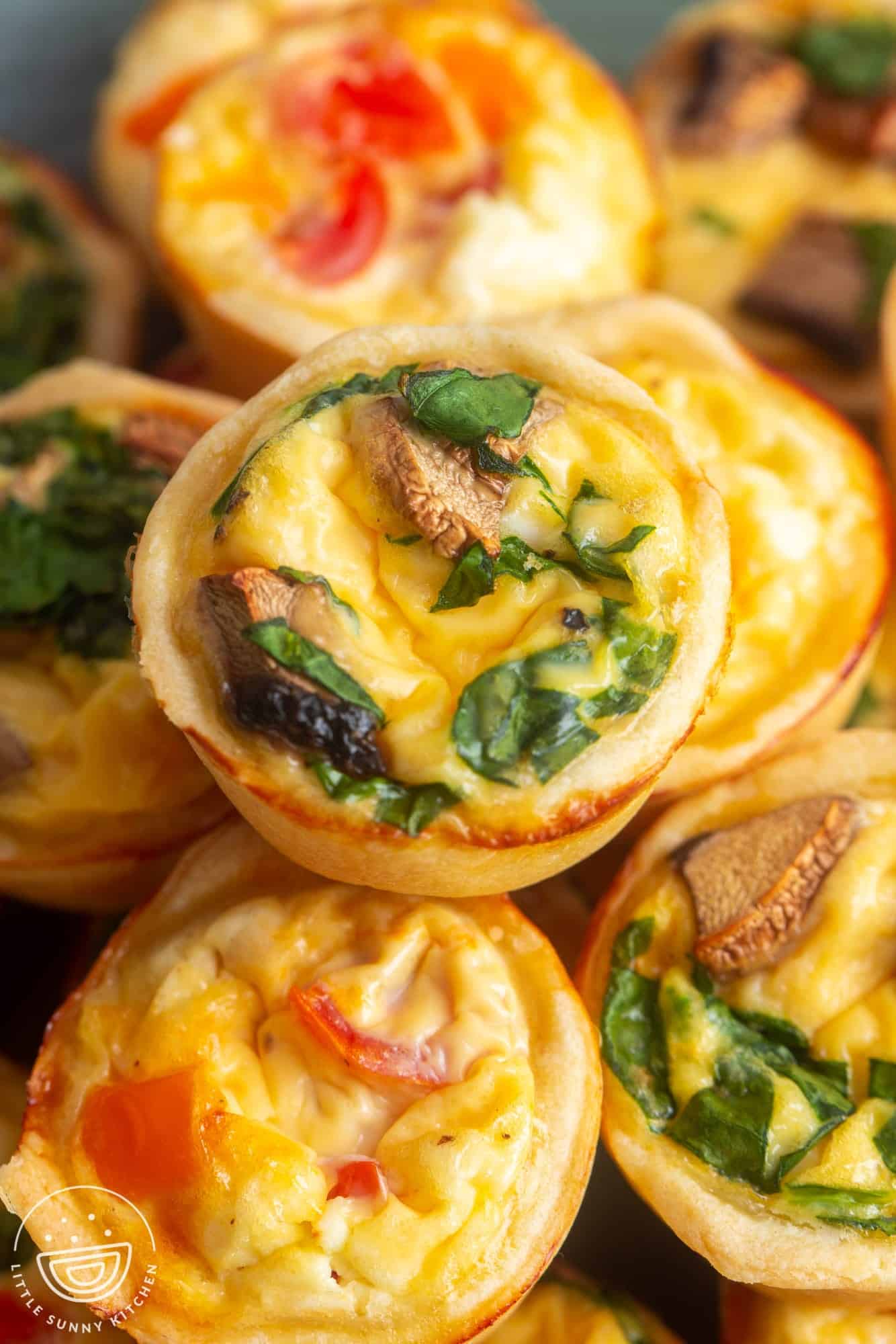 closeup of a pile of mini quiche. the one on top is filled with egg, mushroom, and spinach.