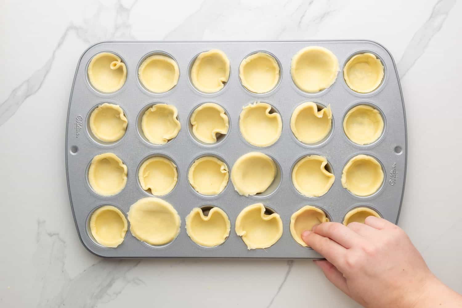 pie crust circles being pressed into the cavities of a mini muffin pan. 