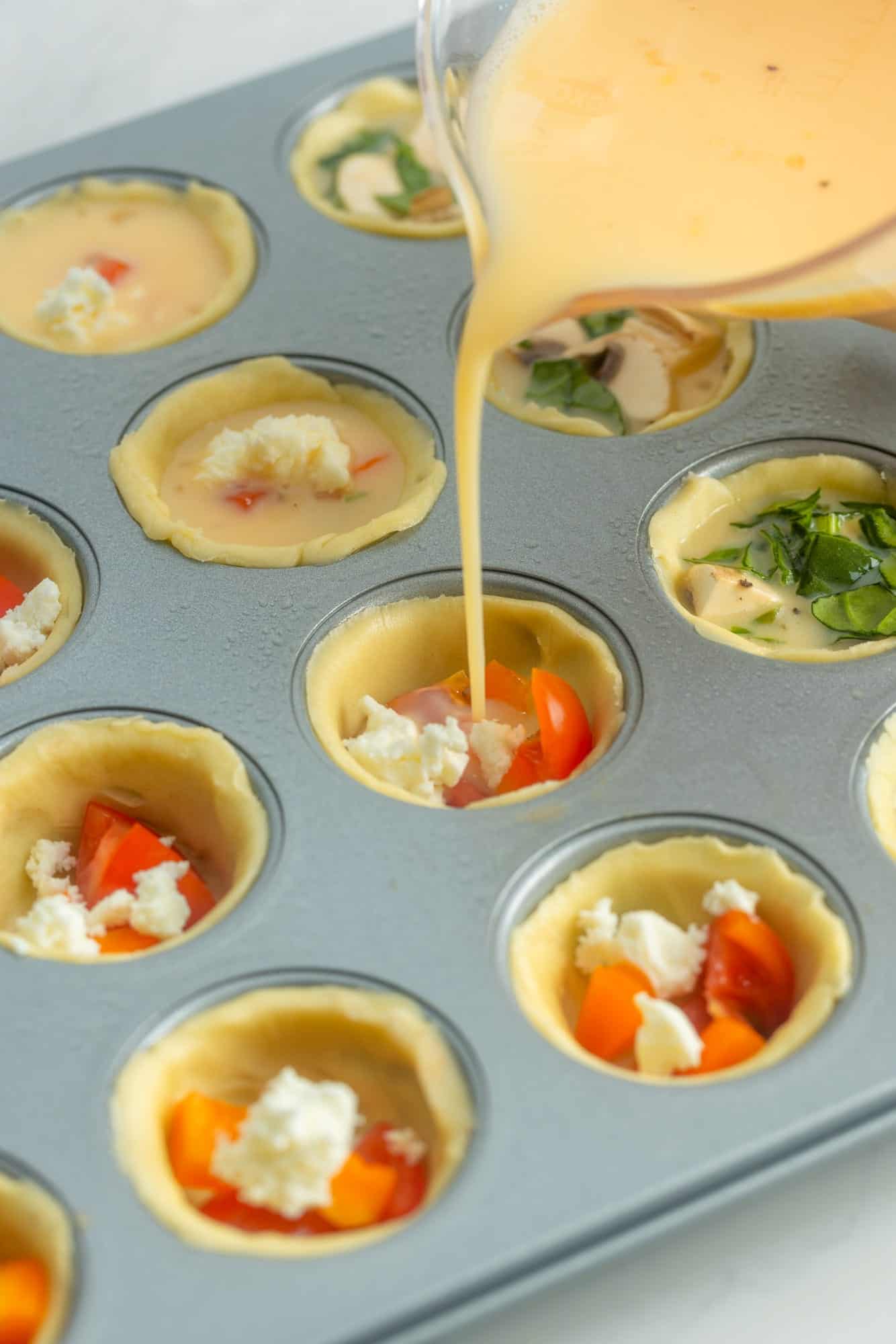 eggs poured over veggies and cheese in a mini muffin pan. 
