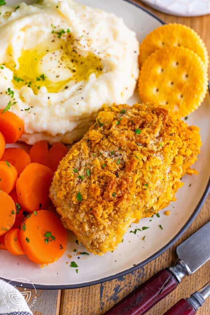 a dinner plate of one crispy breaded pork chop, two ritz crackers, sliced boiled carrots, and mashed potatoes with butter.