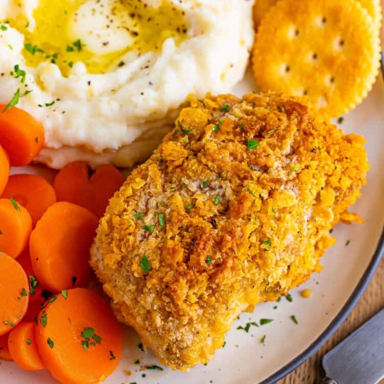 a dinner plate of one crispy breaded pork chop, two ritz crackers, sliced boiled carrots, and mashed potatoes with butter.
