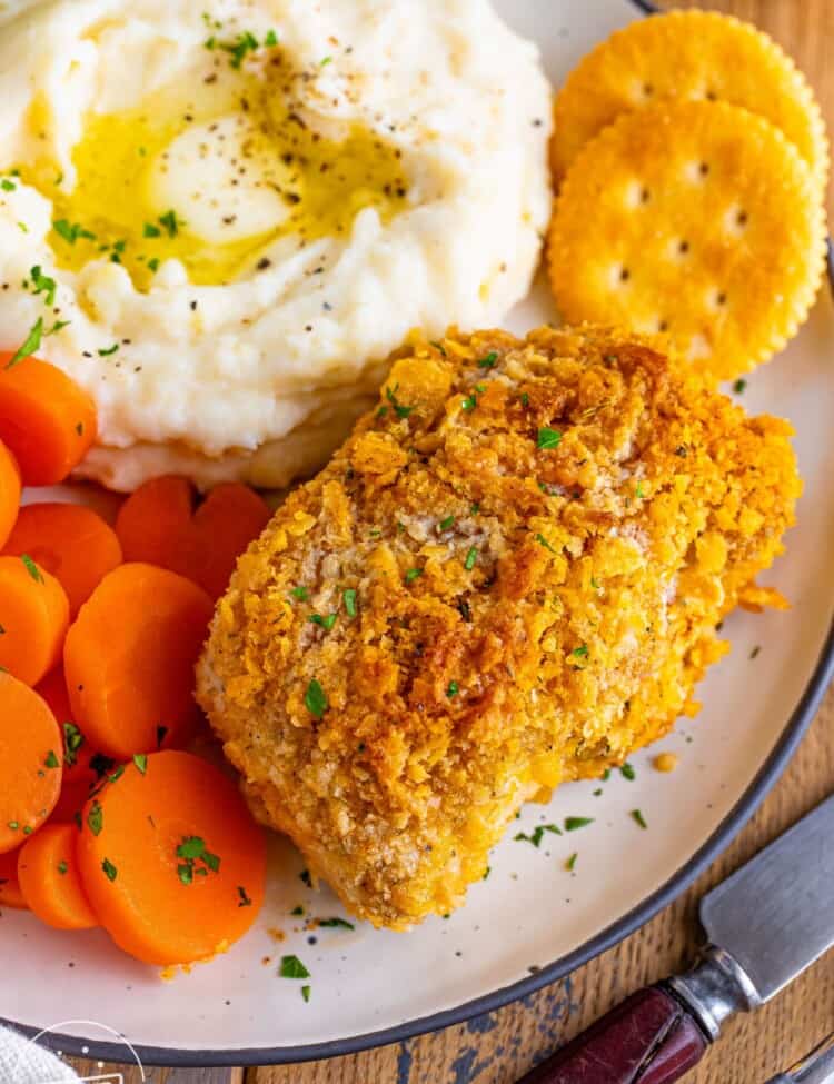 a dinner plate of one crispy breaded pork chop, two ritz crackers, sliced boiled carrots, and mashed potatoes with butter.
