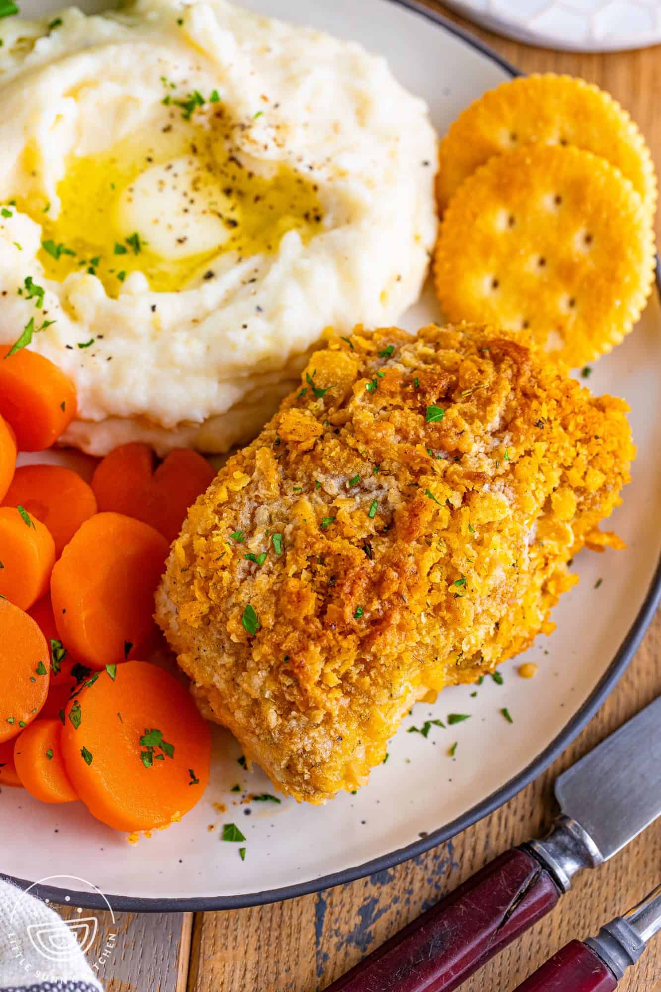 a dinner plate of one crispy breaded pork chop, two ritz crackers, sliced boiled carrots, and mashed potatoes with butter. 