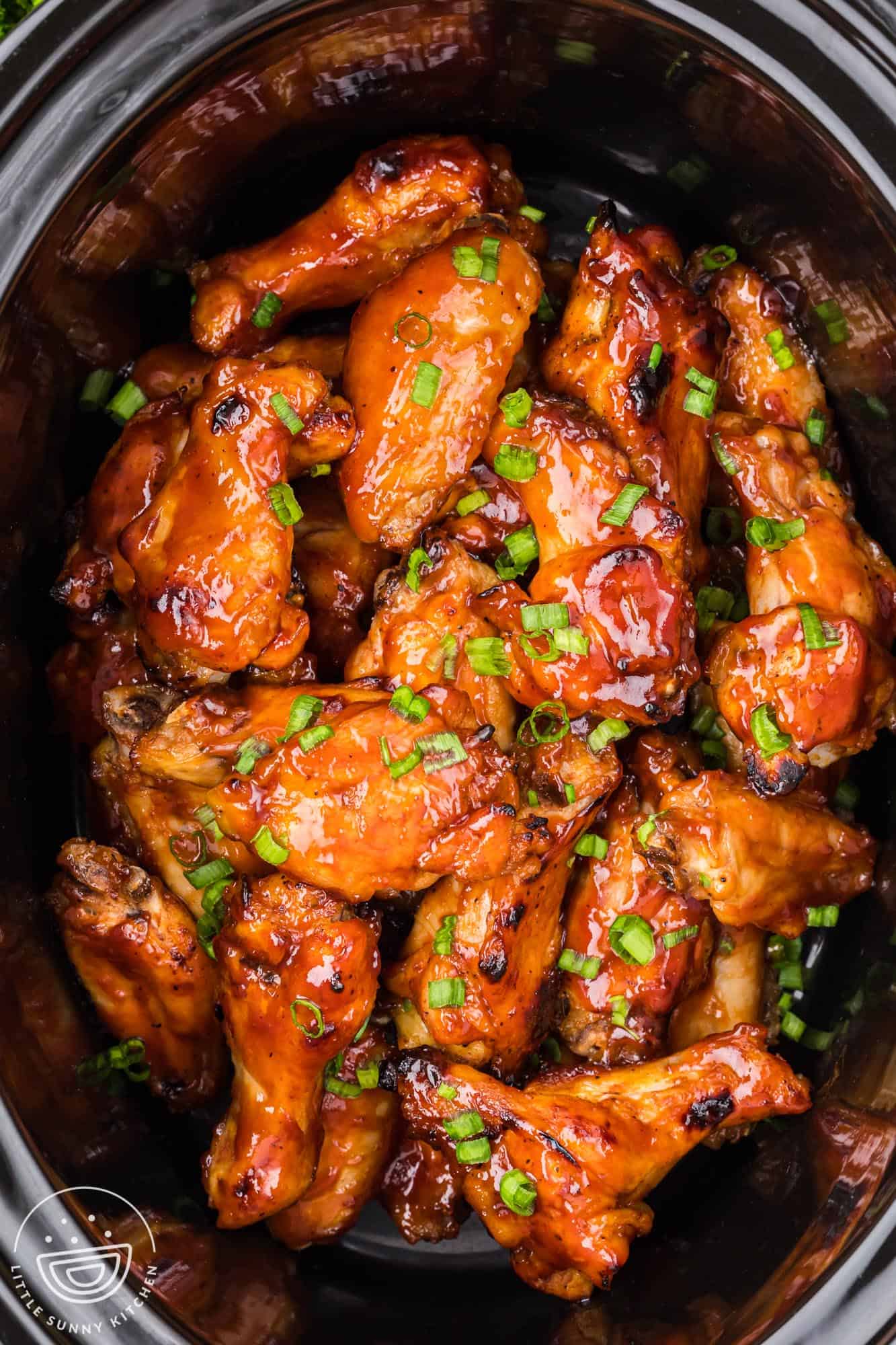 bbq chicken wings in a black slow cooker, viewed from above.