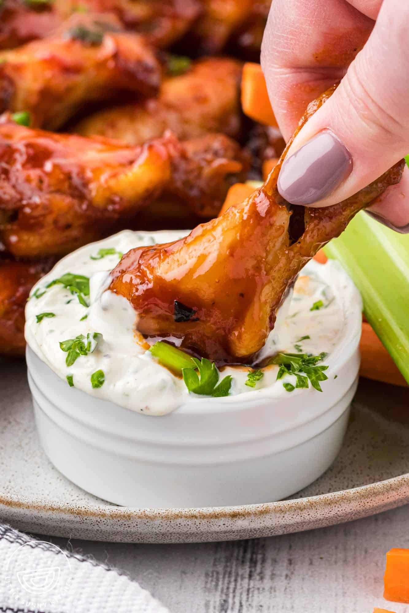 a hand dipping a chicken wing into homemade ranch dip. 