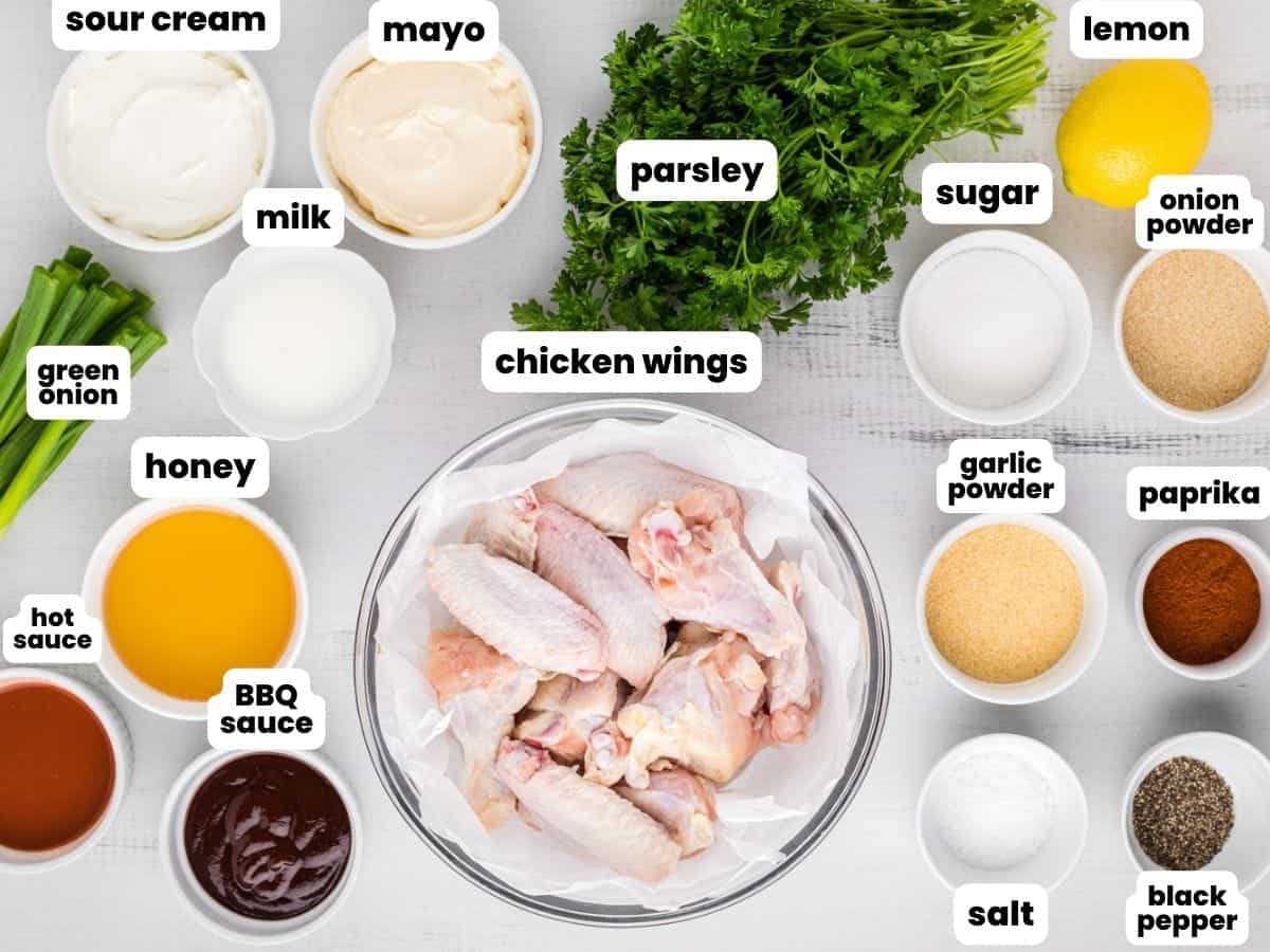 a bowl of raw chicken wing pieces, surrounded by the ingredients needed to cook them in a crockpot with bbq sauce and ranch. 