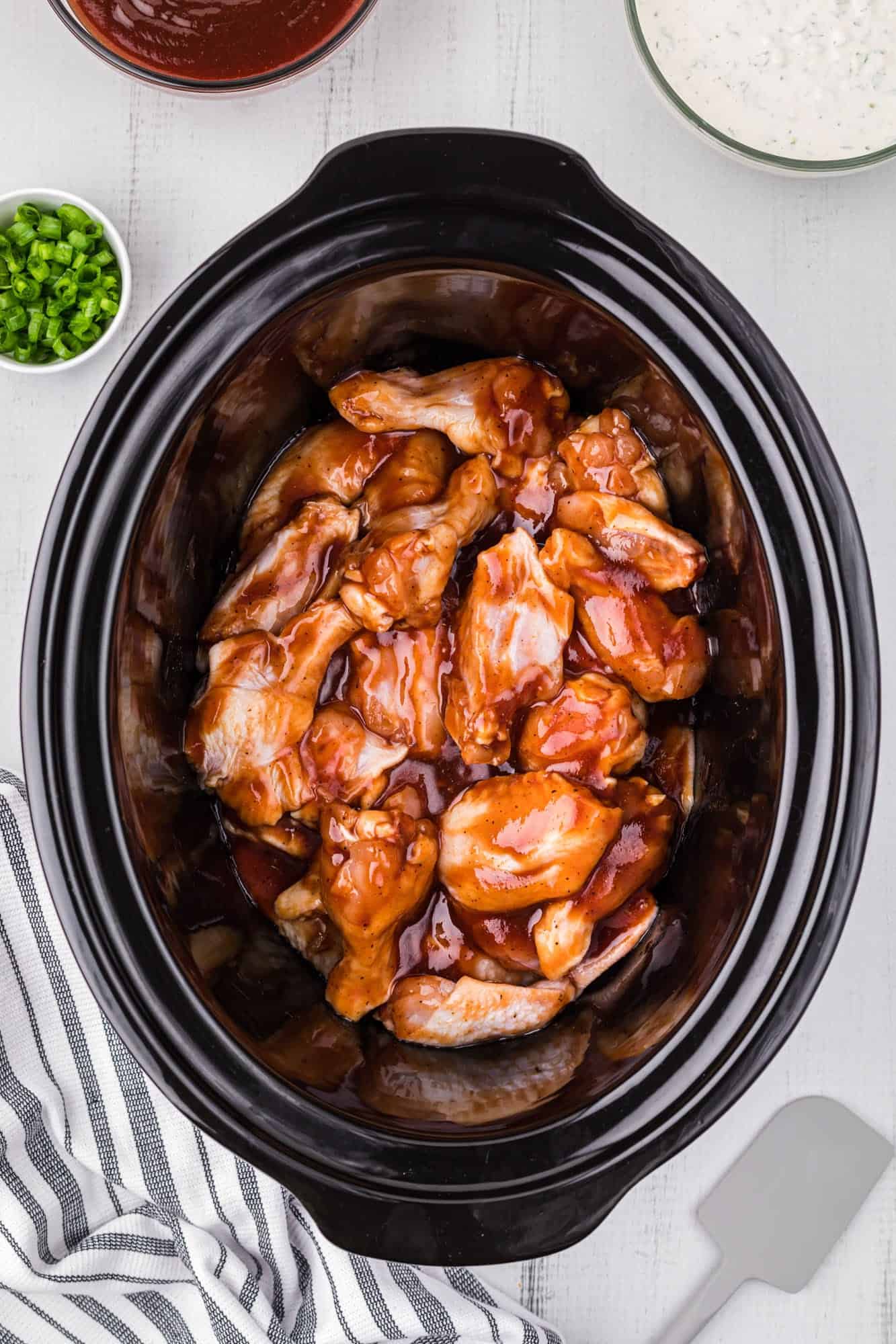 raw chicken wings and bbq sauce in a black oval slow cooker. 