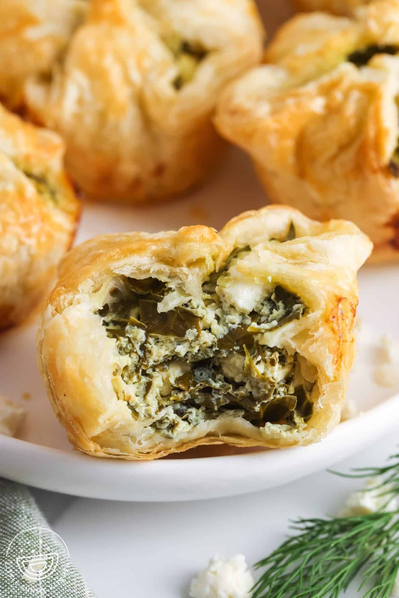 closeup of a homemade spinach puff made with puff pastry sheets and fresh spinach. A bite has been taken to show the filling. 