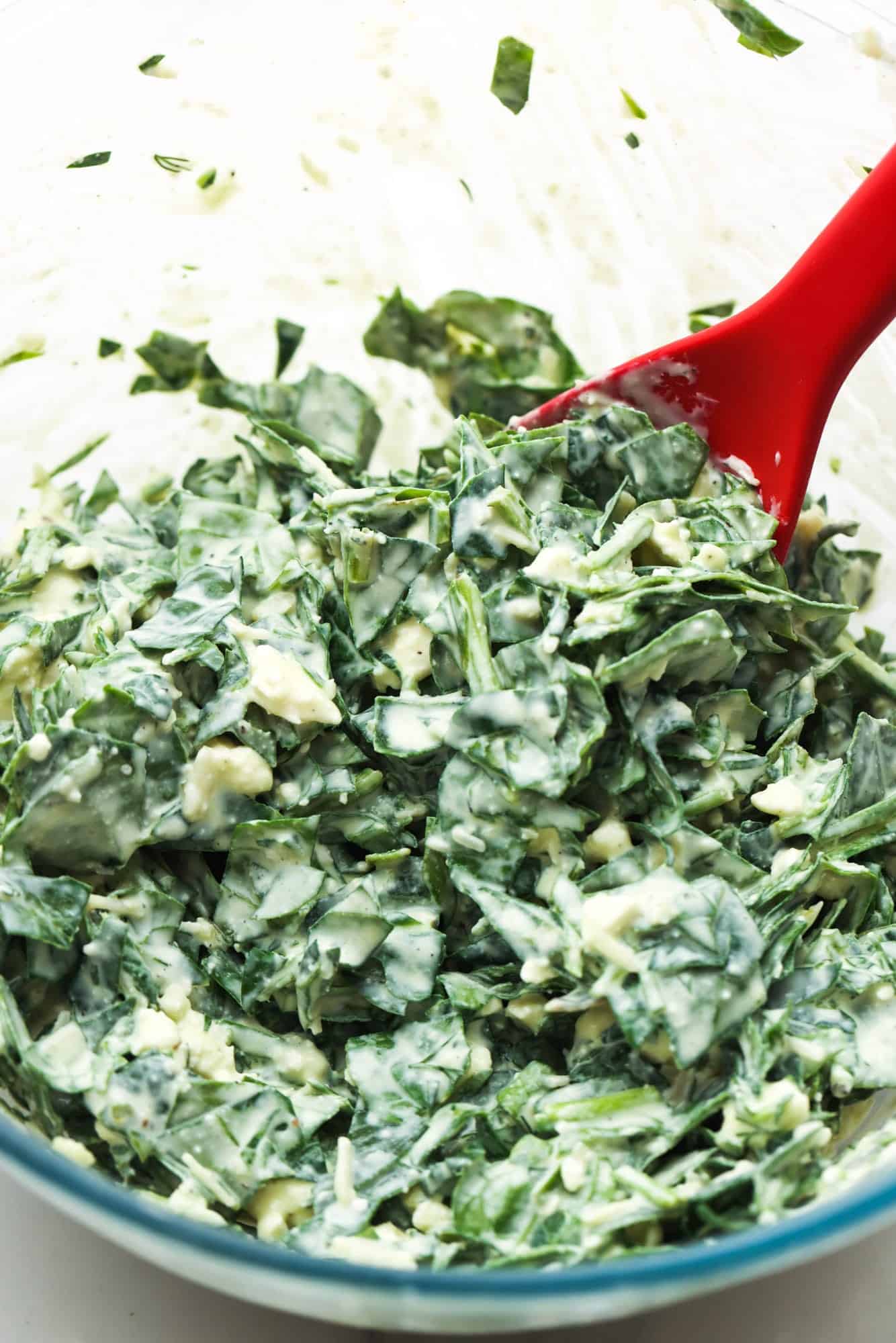 Spinach puff filling made with chopped fresh spinach in a bowl, stirred with a red spoon. 