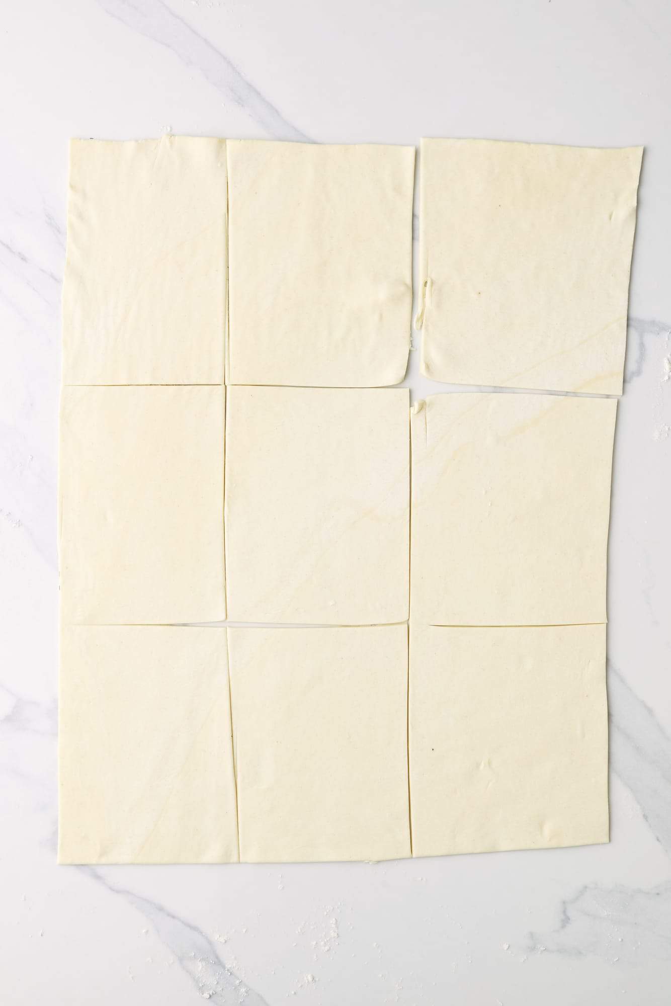 a puff pastry sheet rolled on a marble counter, cut into 9 squares. 
