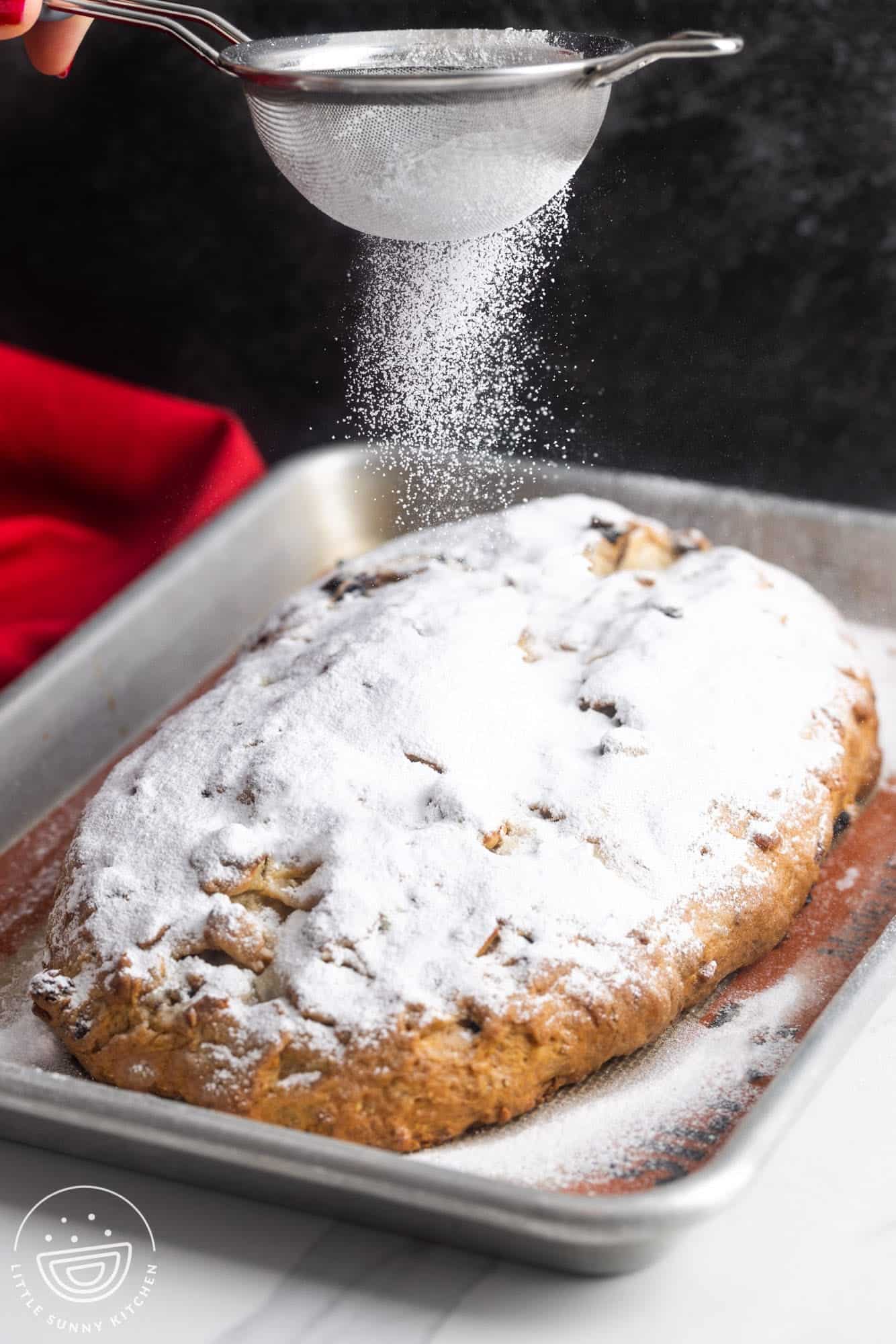 powdered sugar dusted over a loaf of stollen with a small sifter. 