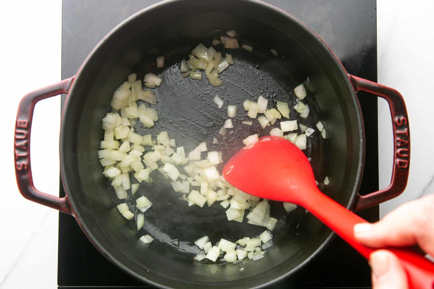 diced onion sauteed in a dutch oven with a red spoon.