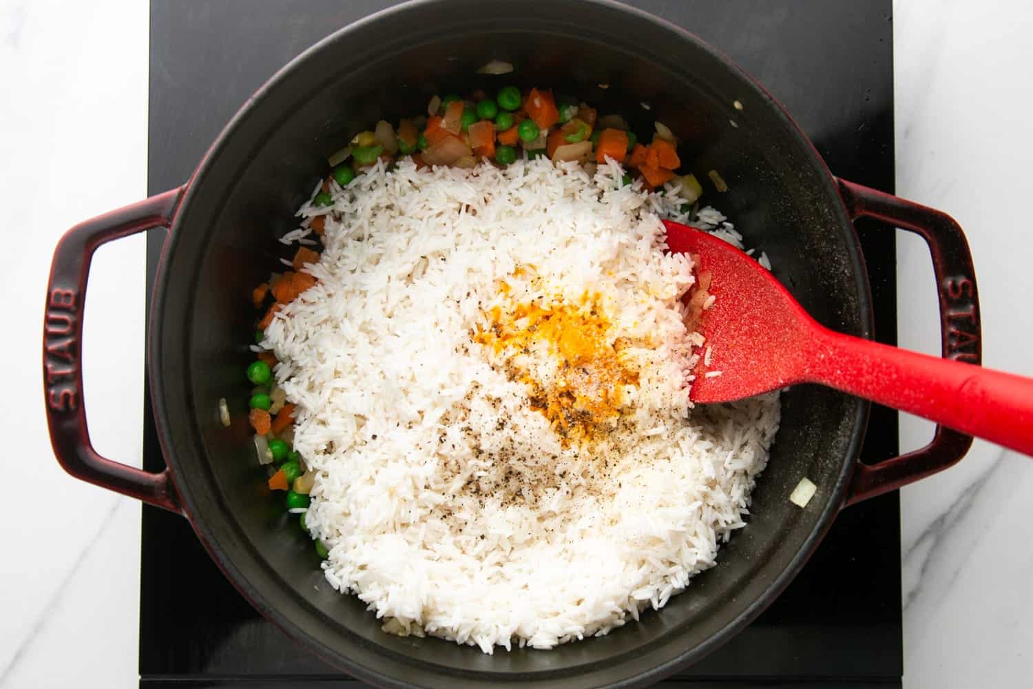 rice and spices added to a saucepan with vegetables.