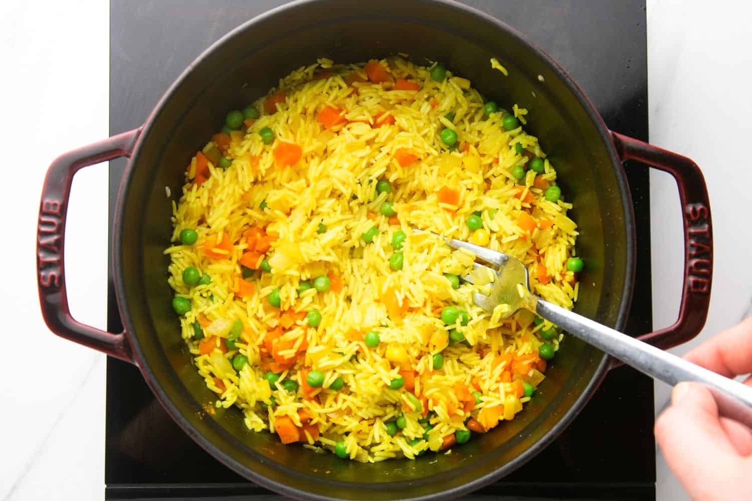 a fork fluffing up rice with mixed vegetables before serving.