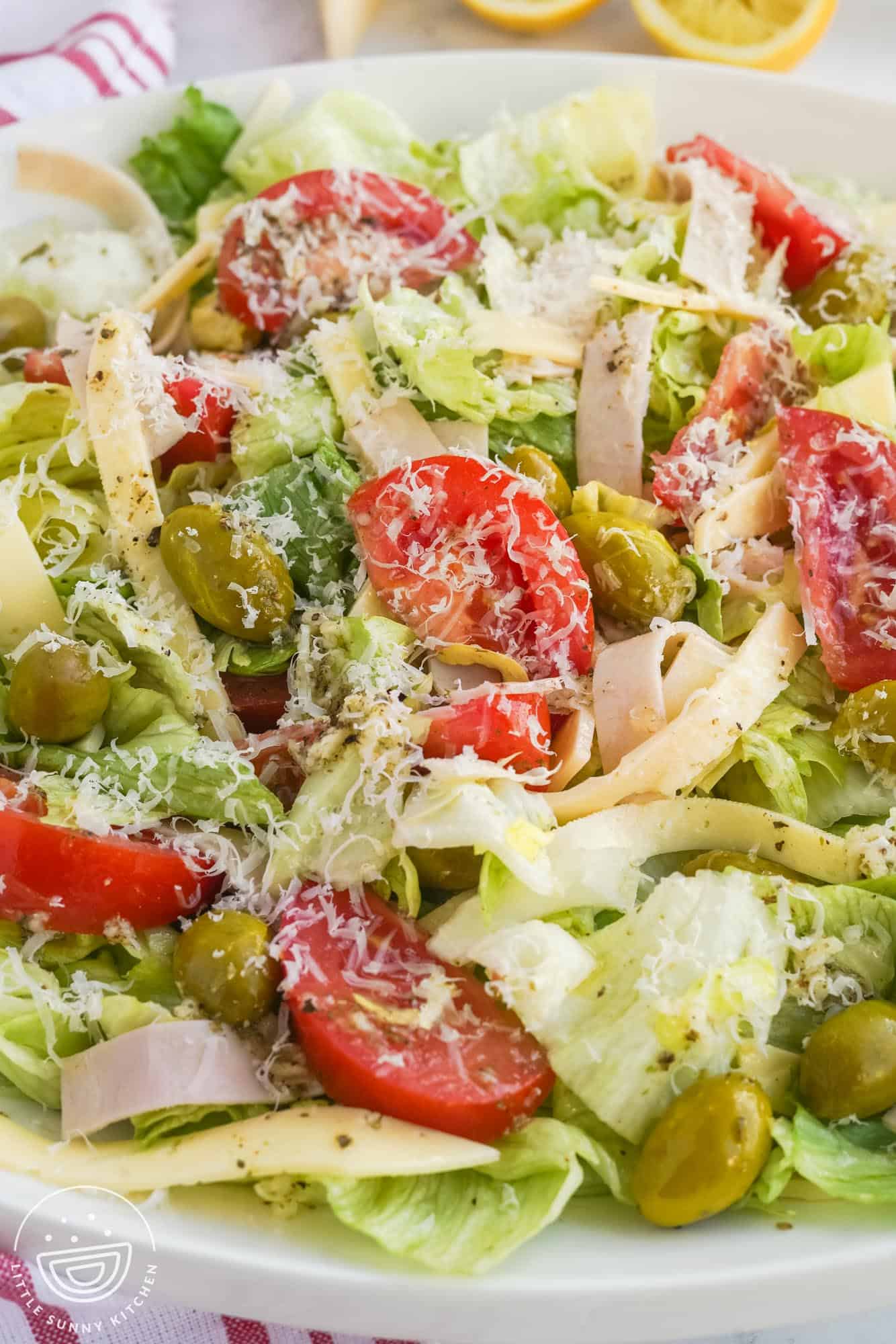 a bowl of salad with olives, tomatoes, cheese, and ham, sprinkled with fresh romano cheese and 1905 dressing.