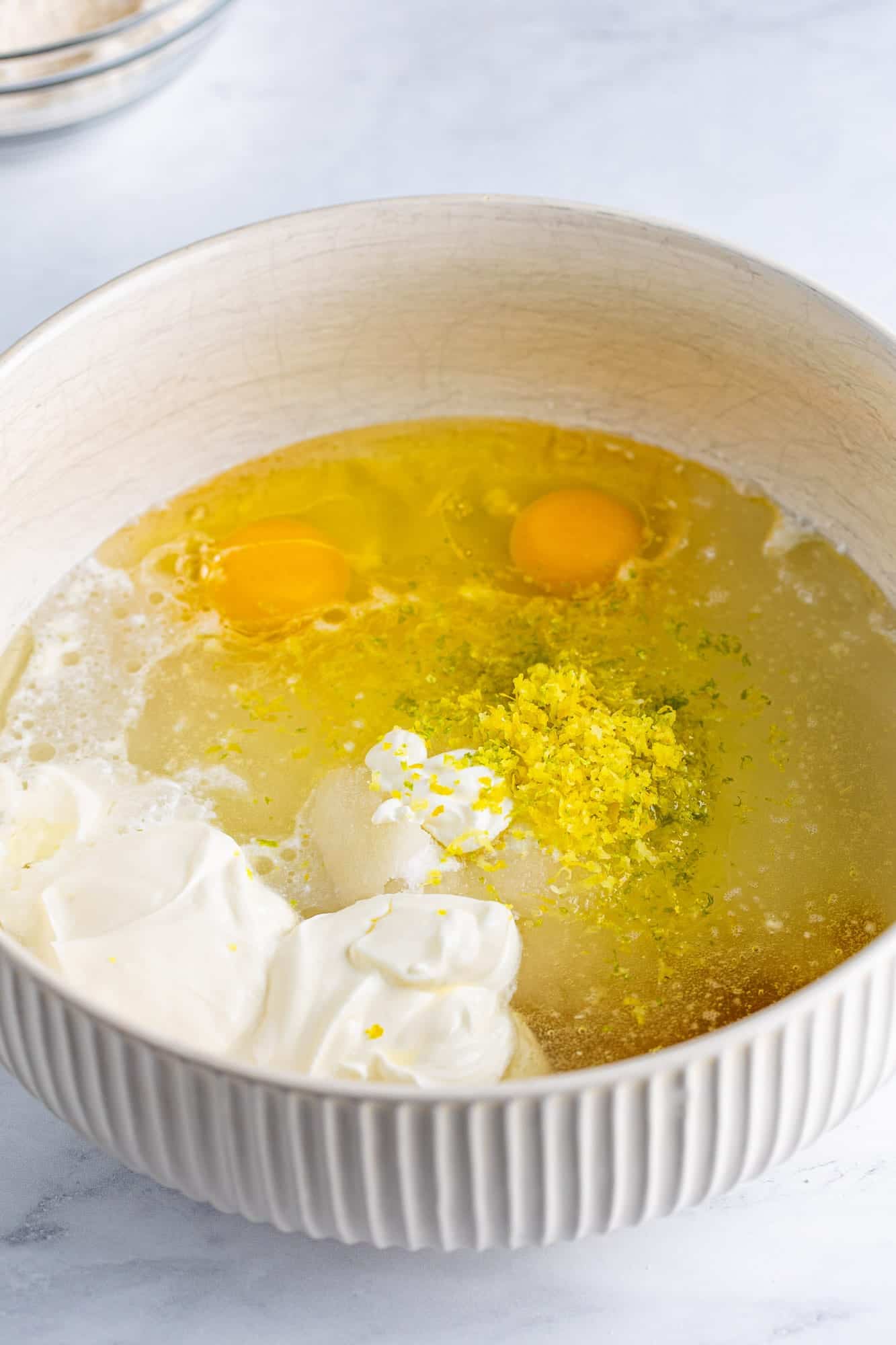 a ceramic mixing bowl holding sour cream, sugar, eggs, oil, lemon zest and lime zest for 7 up cake