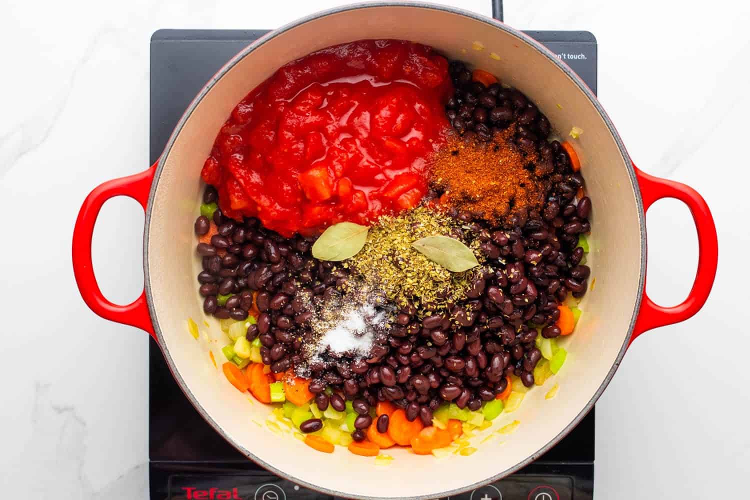 a dutch oven holding beans, vegetables, spices, bay leaves, canned tomatoes.