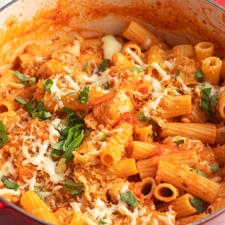 a large dutch oven filled with rigatoni and chicken in a tomato sauce, topped with cheese and breadcrumbs