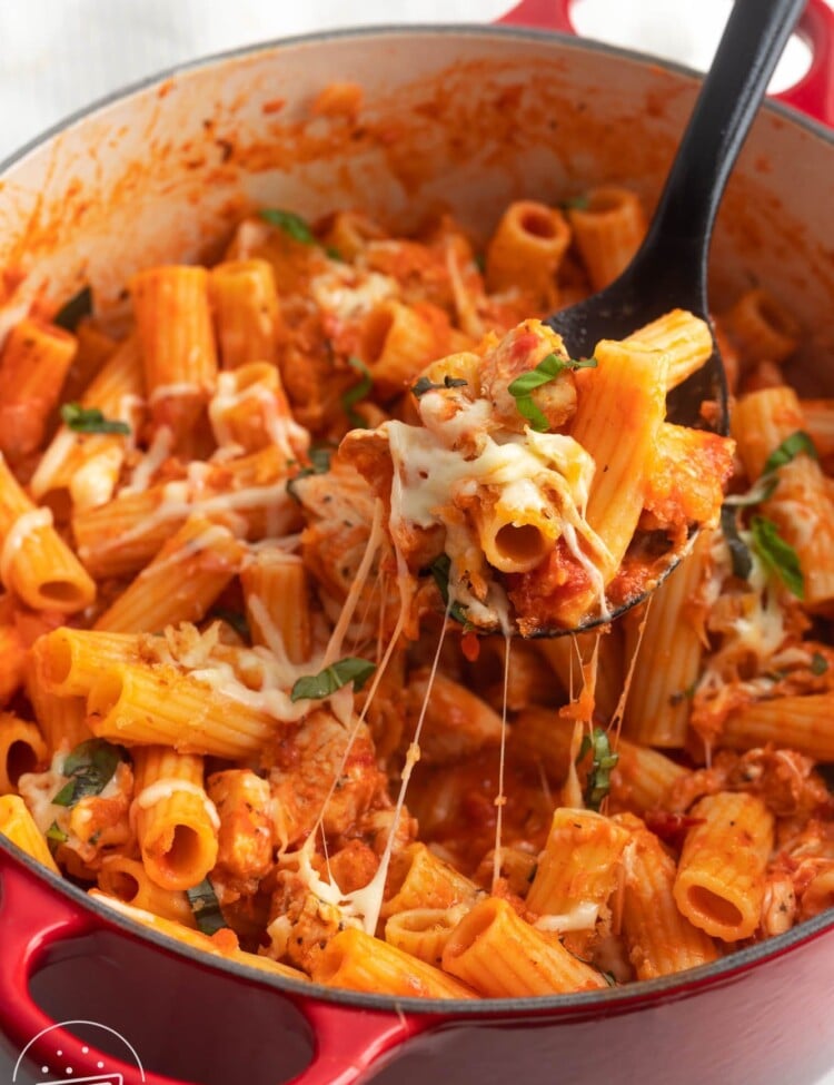 a dutch oven of one pot chicken parmesan pasta. A spoon is lifting some up to show the cheese melt.
