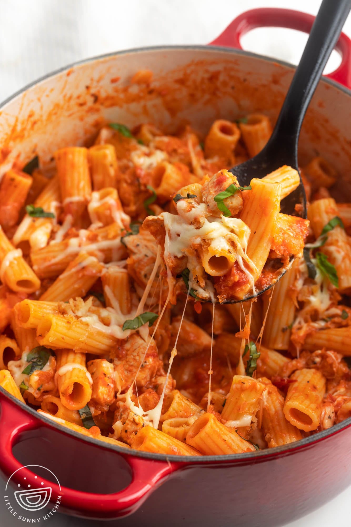 a dutch oven of one pot chicken parmesan pasta. A spoon is lifting some up to show the cheese melt. 