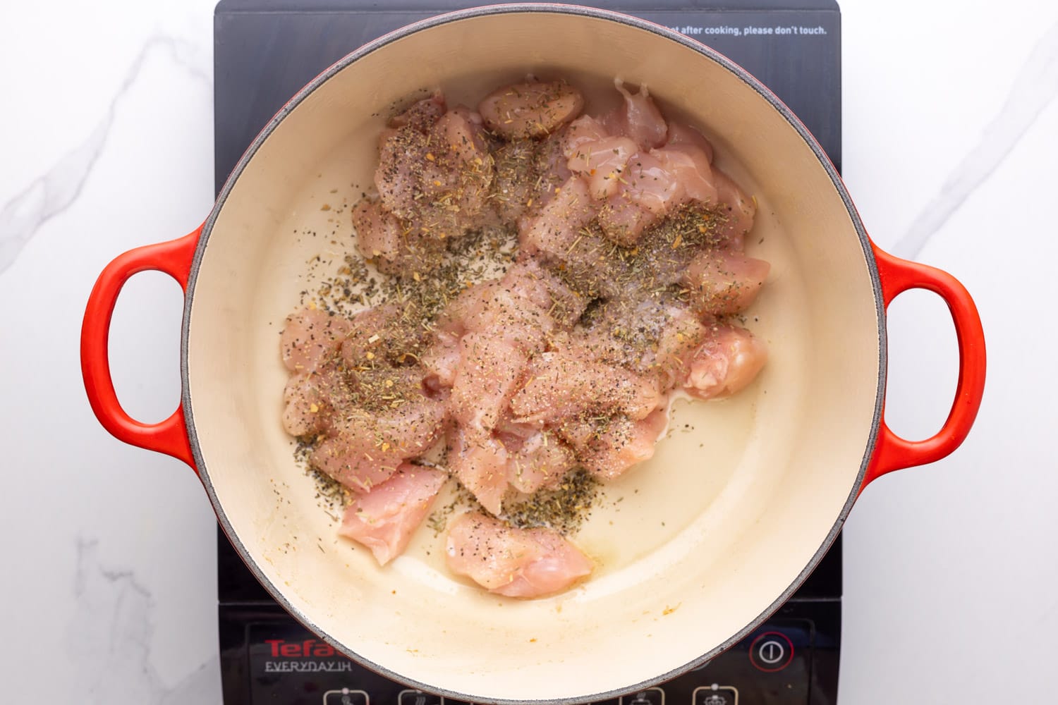 raw diced chicken seasoned with italian seasoning in a dutch oven with oil. 