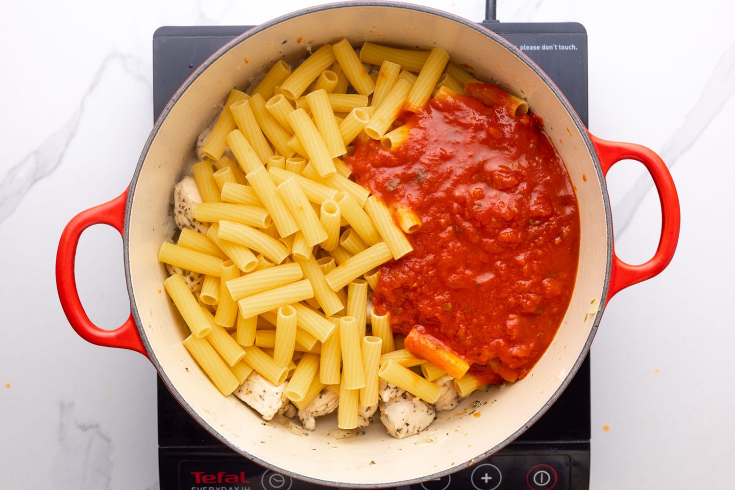 uncooked ziti in a pot with tomato sauce and cooked chicken. 