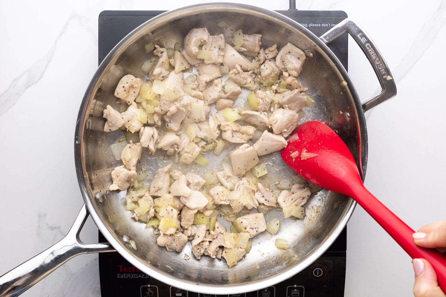 chicken cubes sauteed in a skillet with onions, garlic, and ginger.