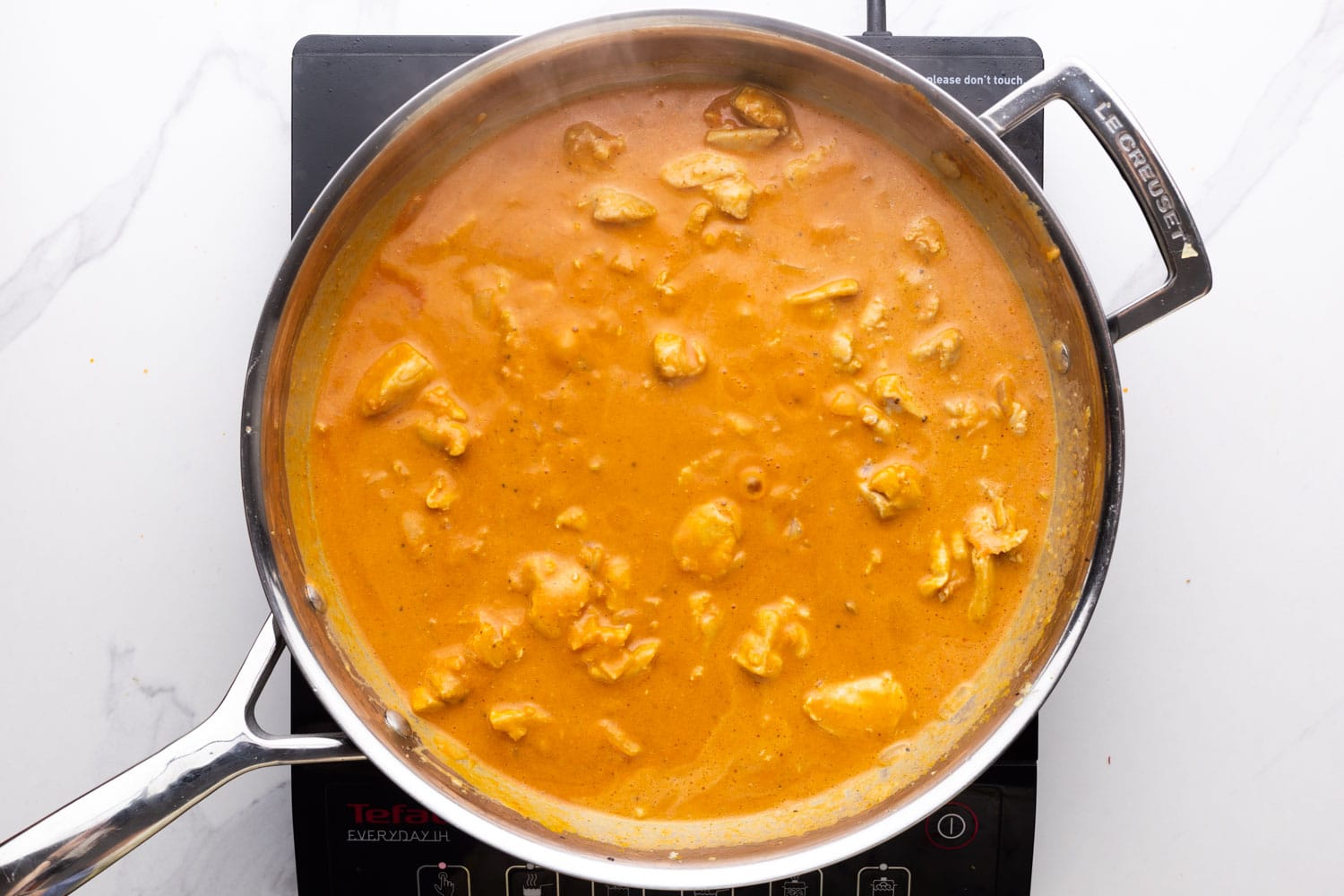 chicken coconut curry simmering in a stainless steel skillet.