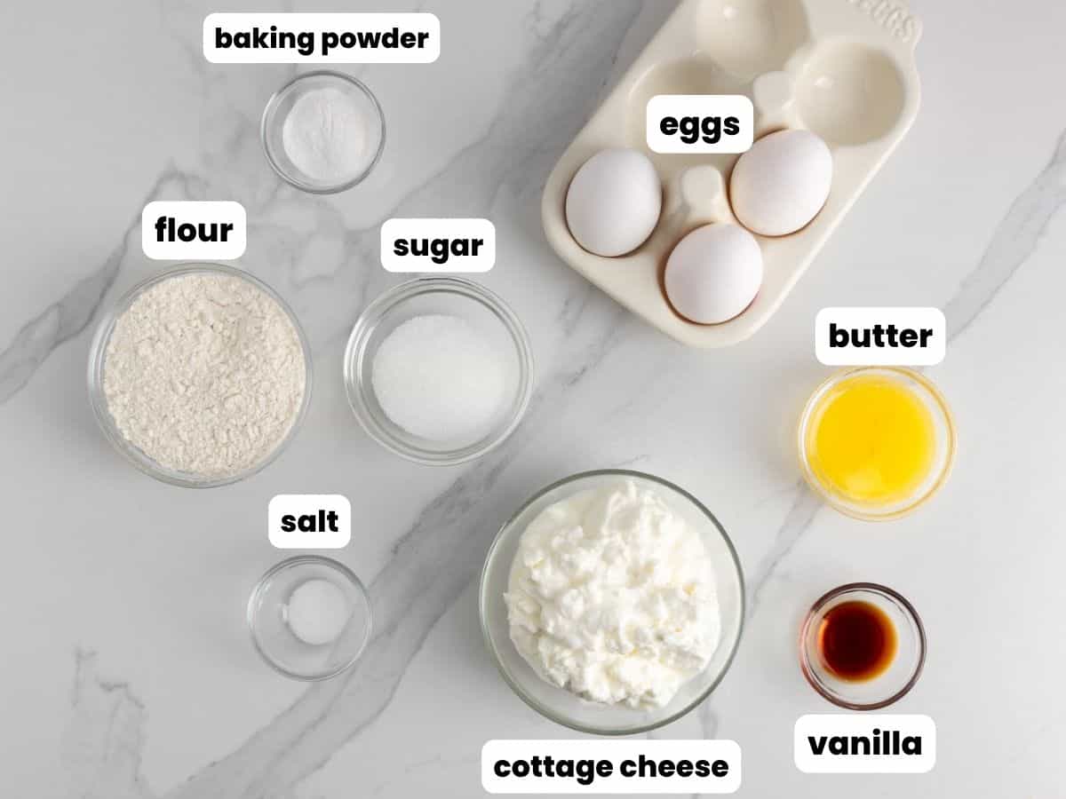 Ingredients for cottage cheese pancakes, all in separate bowls, arranged on a marble counter. 