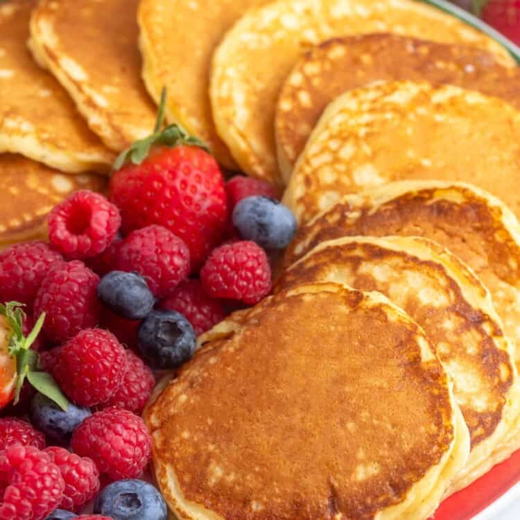 a large red round platter holding pan fried cottage cheese pancakes that are arranged in a circle around the plate. In the center are fresh mixed berries.