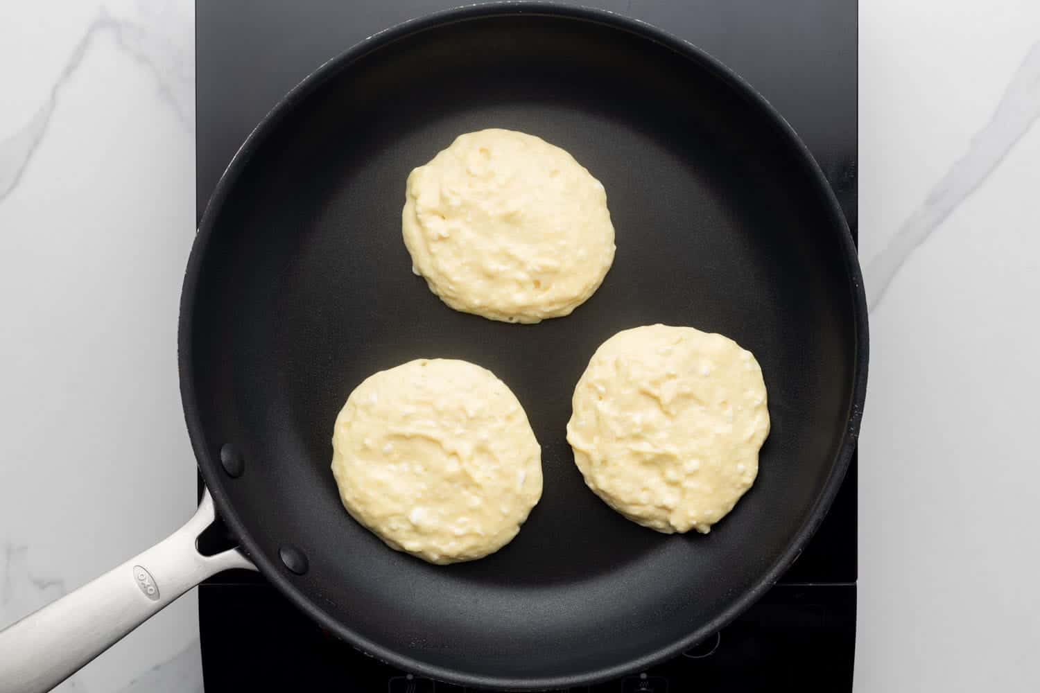 a black non-stick skillet holding three uncooked pancakes with cottage cheese in the batter.