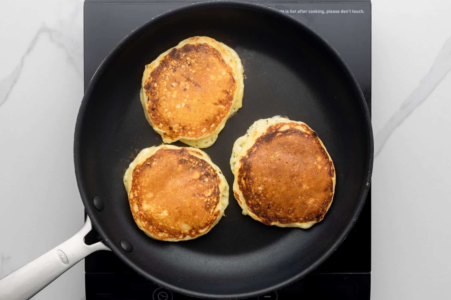 three small cottage cheese pancakes flipped over in a non-stick pan.