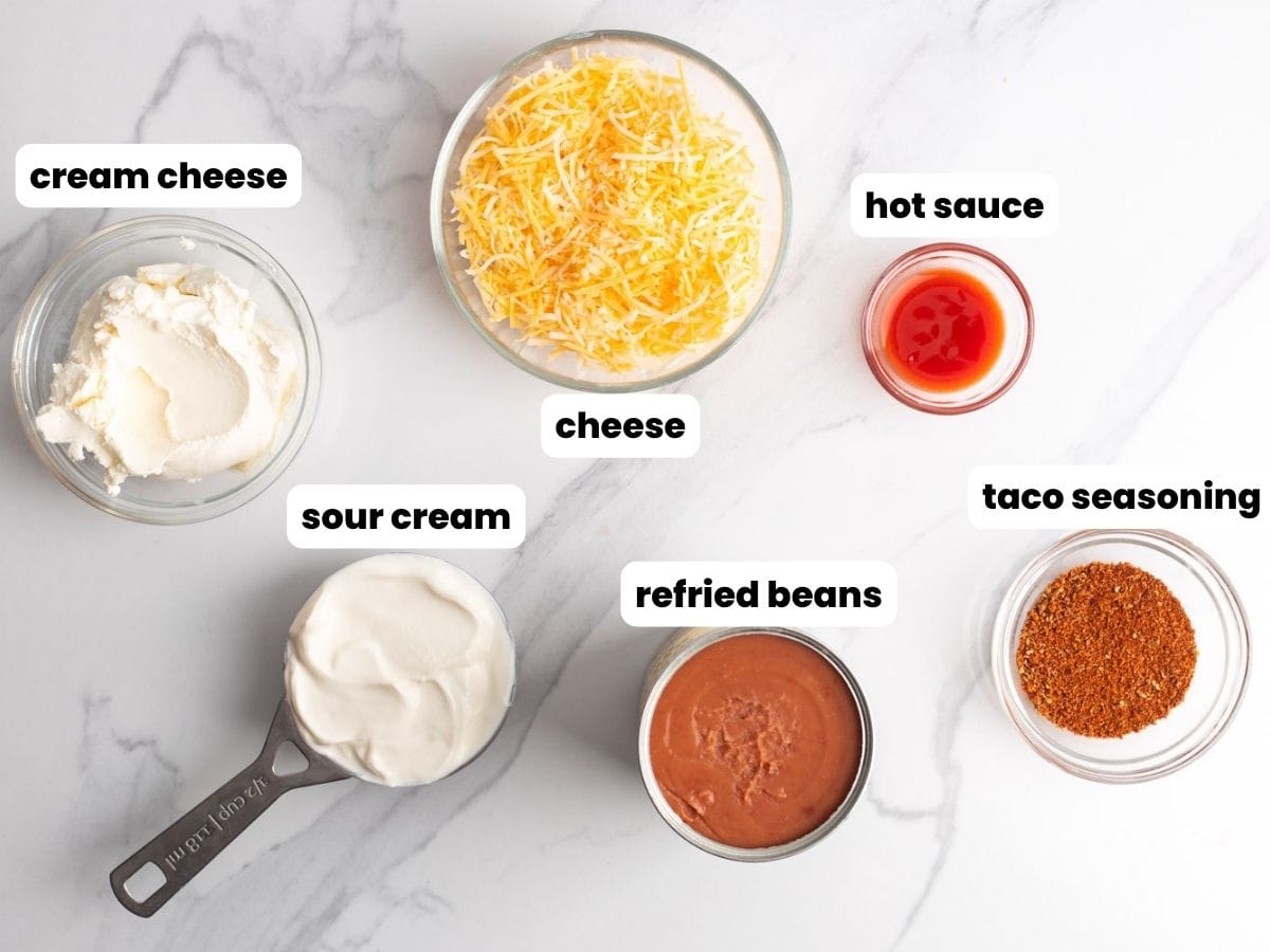 six ingredients needed to make hot cream cheese bean dip, including refried beans, cheese, and taco seasoning.