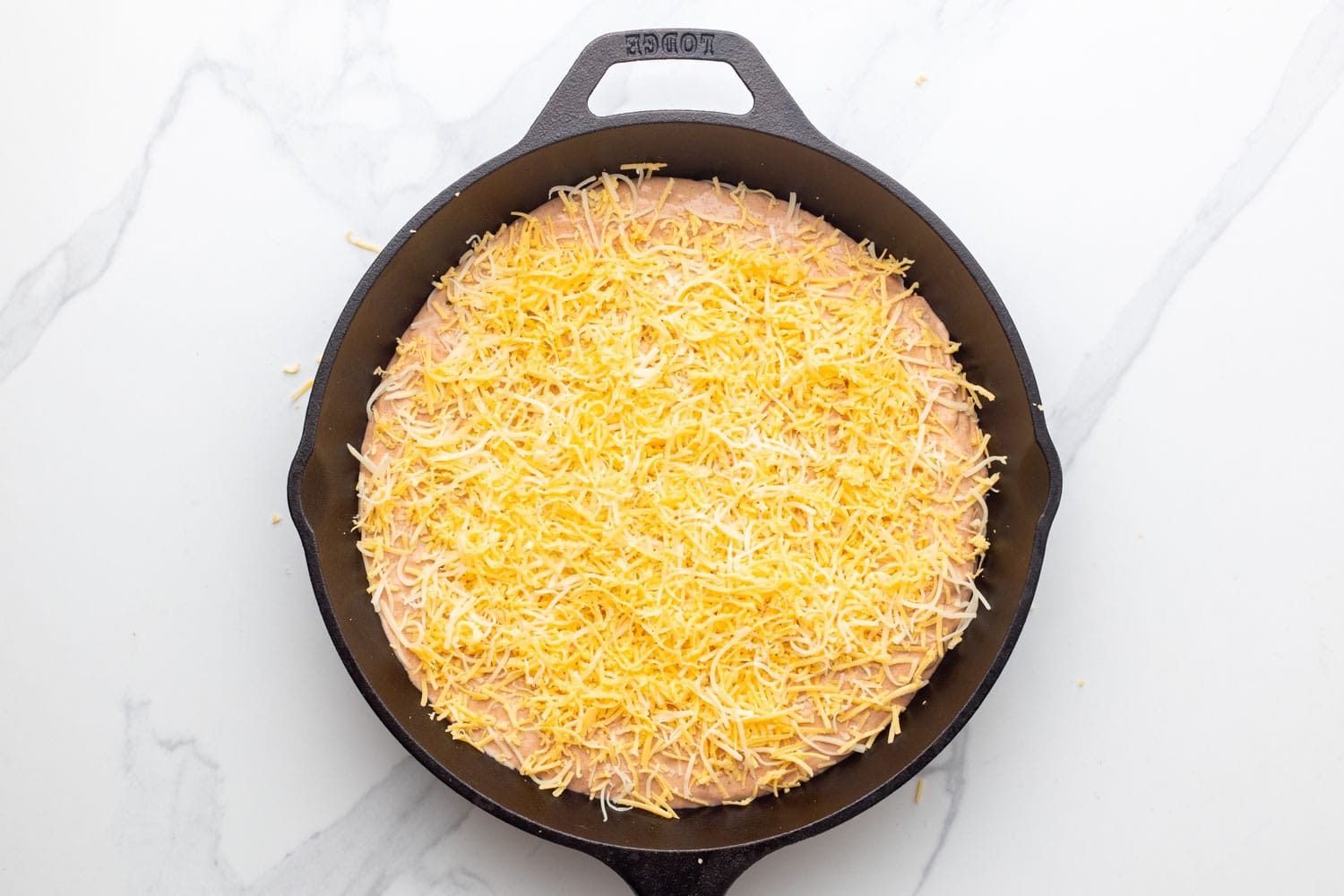 bean dip in a skillet, topped with shredded mexican cheese. 