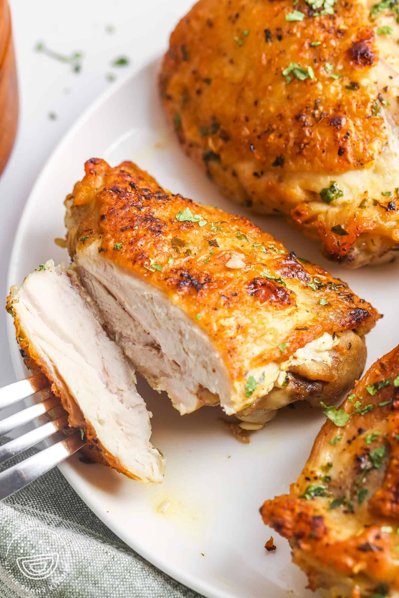 a plate of slow cooker chicken thighs. A fork is taking a slice from the side of one.