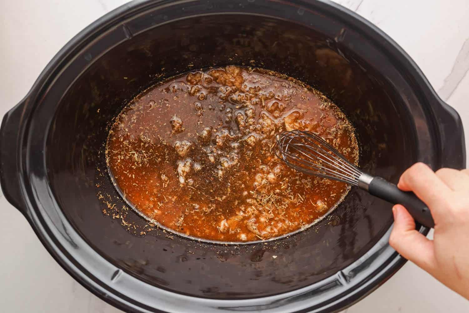 broth with seasonings added to a black slow cooker, stirred with a whisk.