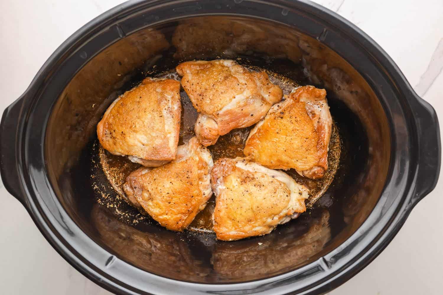 browned chicken thighs added to a slow cooker of sauce.