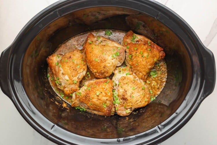 bone in skin on chicken thighs arranged in a slow cooker.
