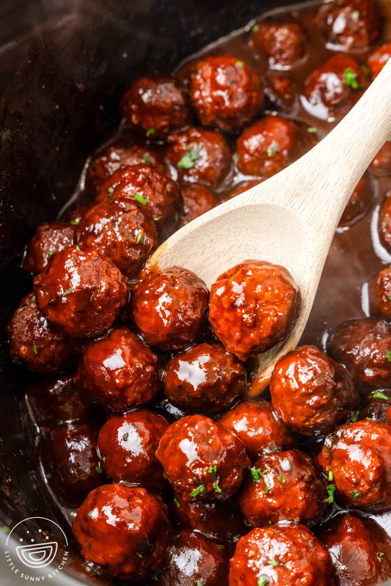 Crockpot grape jelly meatballs in the slow cooker with a serving spoon
