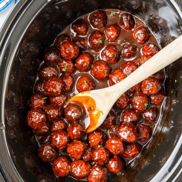 Overhead shot of grapejelly meatballs in the slow cooker with a serving spoon