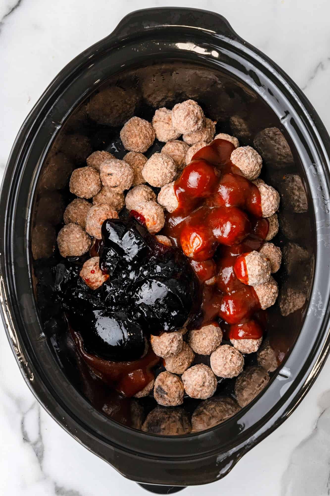 Overhead shot of a slow cooker with meatballs, bbq sauce, and grapejelly sauce.