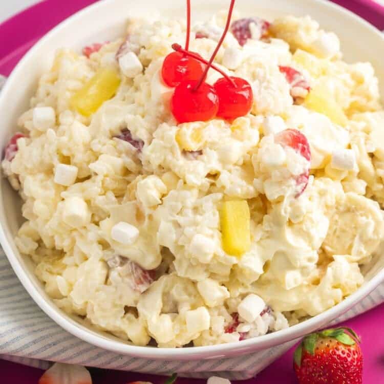 a hot pink platter holding a large bowl of glorified rice, topped with mini marshmallows and maraschino cherries.