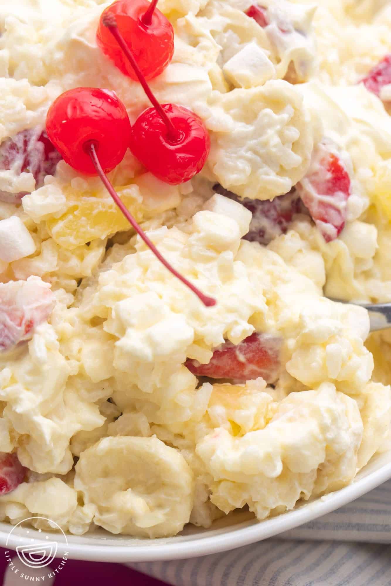closeup of a bowl of creamy glorified rice with bananas, strawberries, and pineapple, topped with three stemmed cherries.